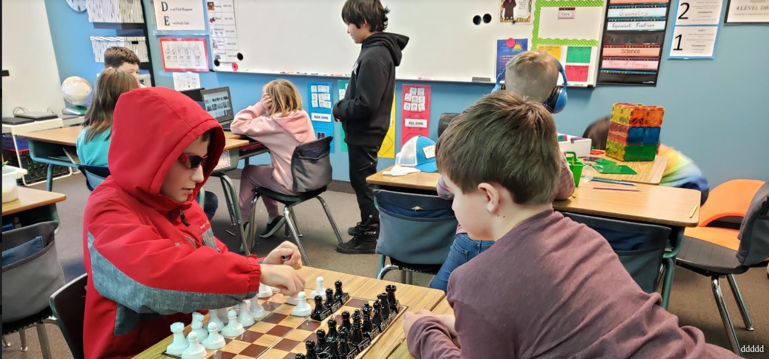 Students play a game of chess together in a lively classroom environment.